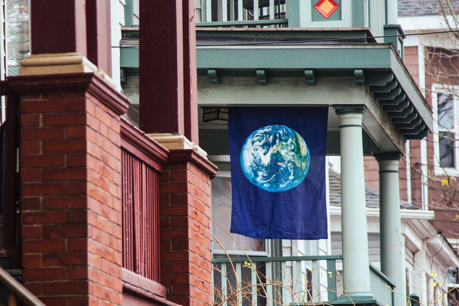 Flag displaying Earth hangs outside a porch, surrounded by brick columns and Victorian-style building details.