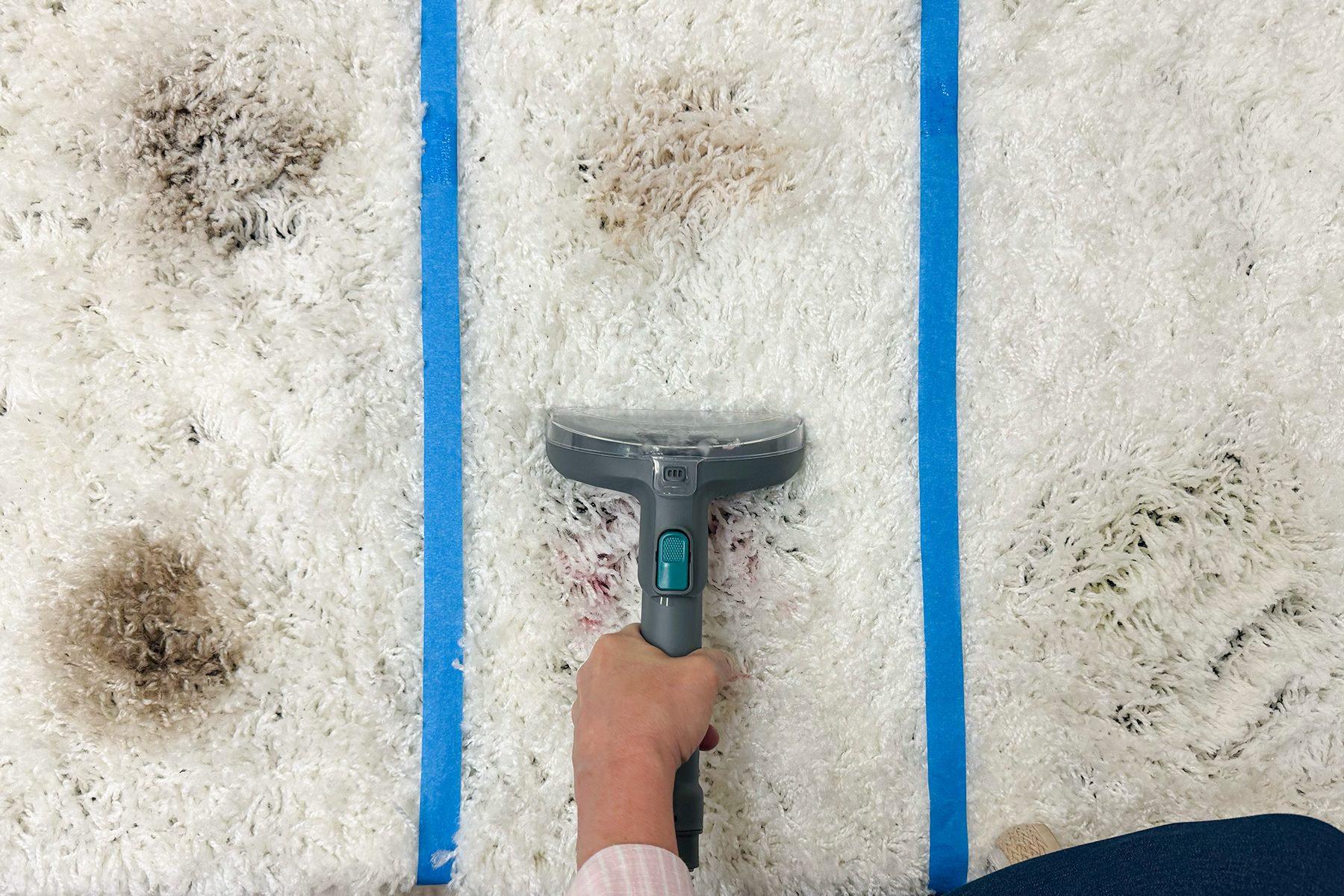 Vacuum cleaner removes dirt on a white carpet sectioned by blue tape lines.