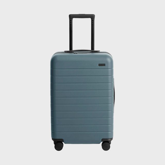 Suitcase stands upright, handle extended, on white background. Four wheels support it. 