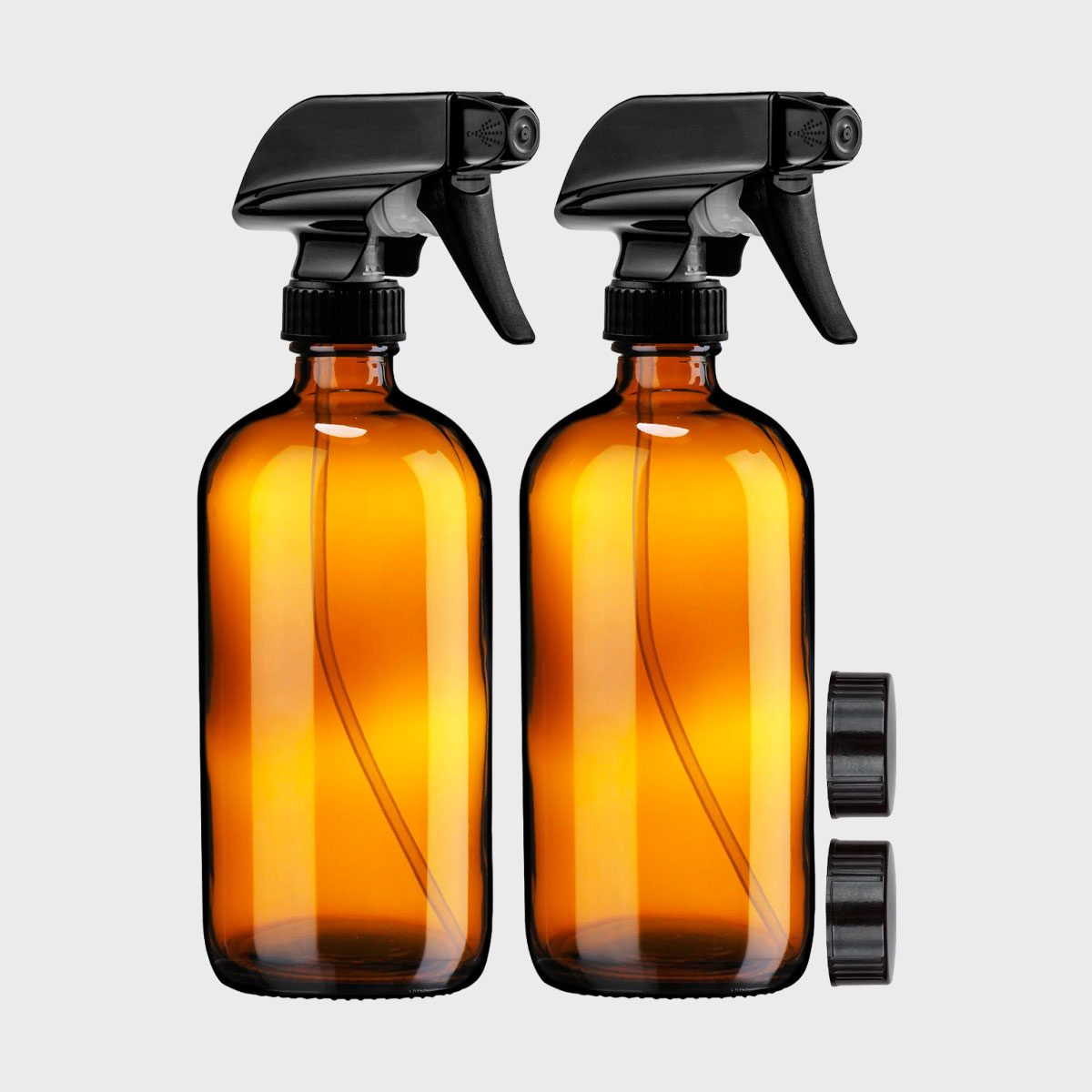 Two amber spray bottles with black triggers are upright against a plain gray background, accompanied by two additional black caps.