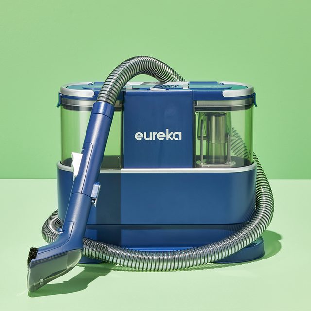 Blue vacuum cleaner sits with hose attached, displayed against a vibrant green background. The word 