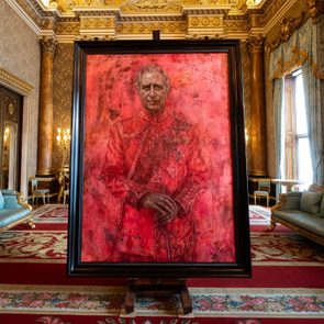 A large, red-tinted portrait stands on an easel in an ornate room with luxurious sofas and elaborate golden decor.