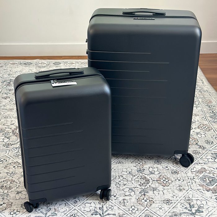 Two black suitcases stand on a patterned rug in a room.