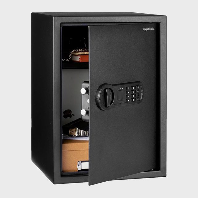 Safe stands open, revealing watches and boxes; keypad lock on the front. Interior items include watches and bracelets, set against a plain background.