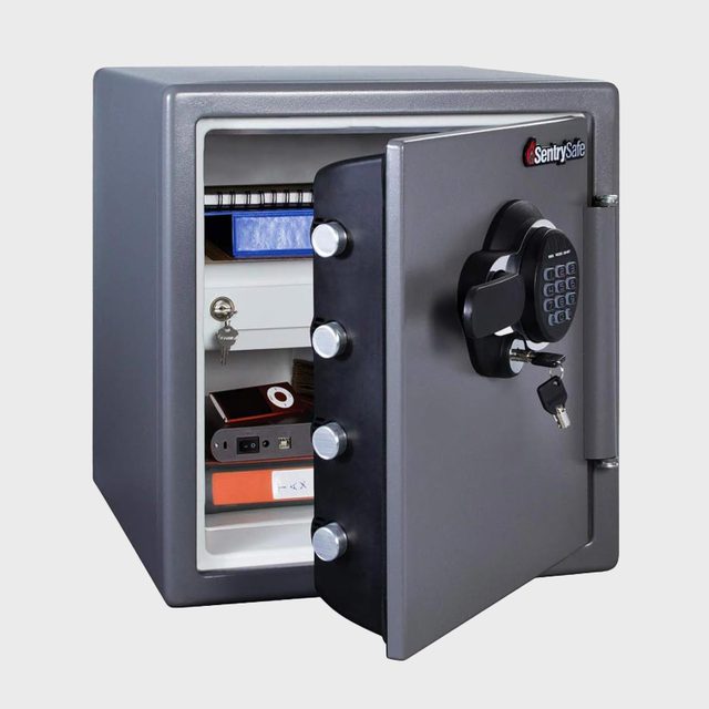Gray safe stands open, revealing shelves holding documents and electronics. A keypad and key are visible on the door.