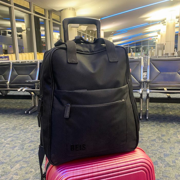 Black bag resting on a pink suitcase in an airport terminal with empty seats and soft overhead lighting. Text: 