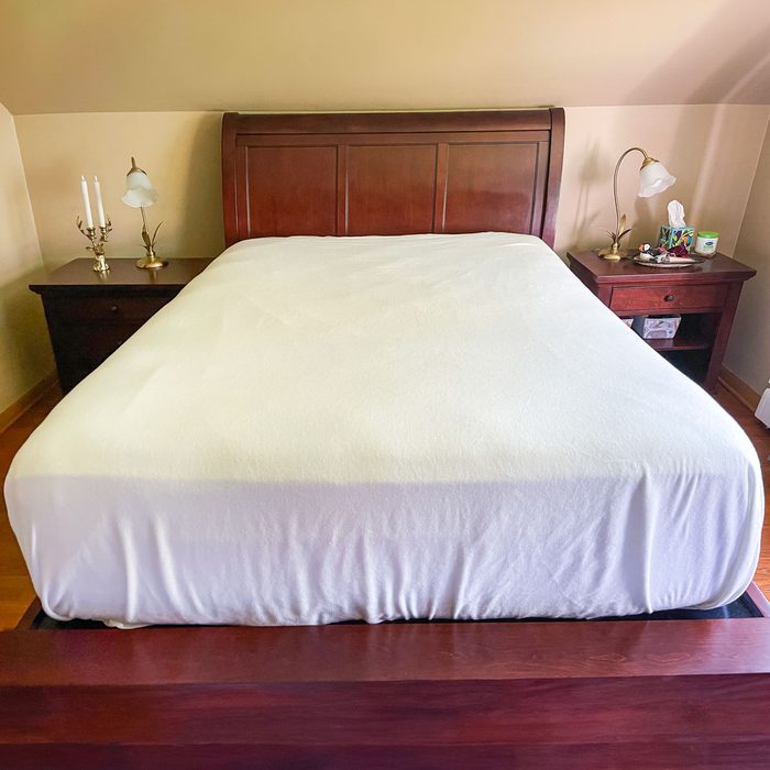 Bed sits neatly in a bedroom, flanked by wooden nightstands with lamps, candles, and assorted items on polished surfaces.
