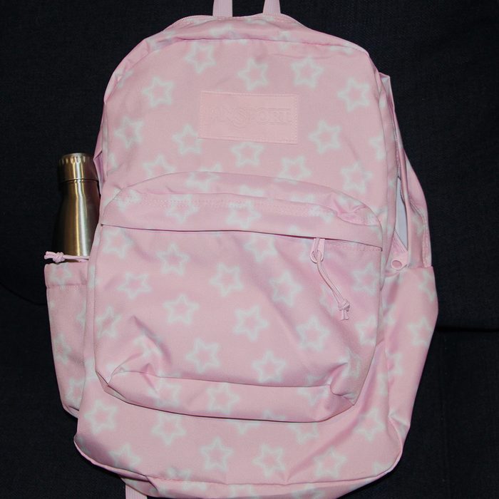 Pink backpack with white stars, holding a stainless steel water bottle, sits against a dark background.