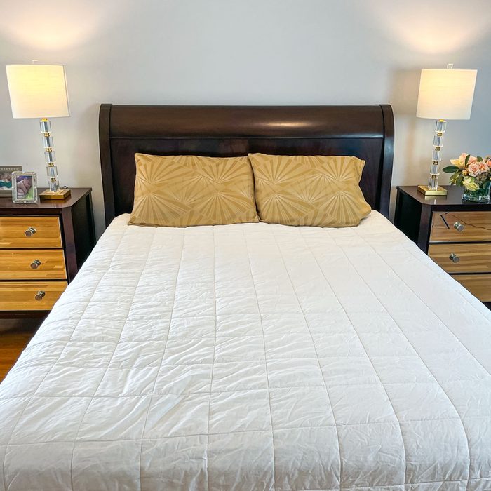 A bed with a white cover, adorned with two beige pillows, flanked by wooden nightstands with lamps in a softly lit bedroom.