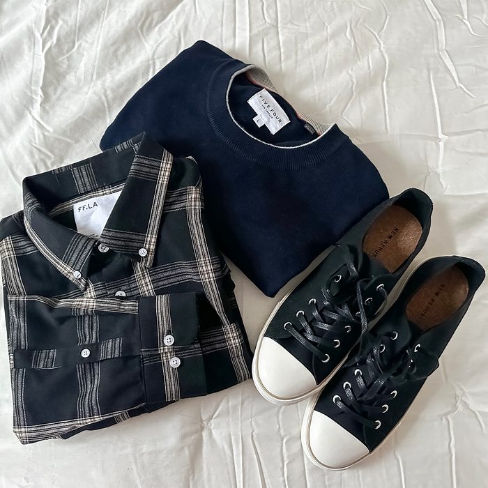 Shirt folded beside a sweater and shoes on a wrinkled, light-colored fabric surface.