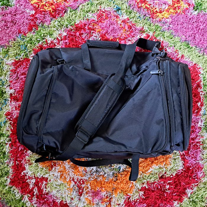 Black duffel bag resting on a colorful, textured rug with red, green, and orange hues.