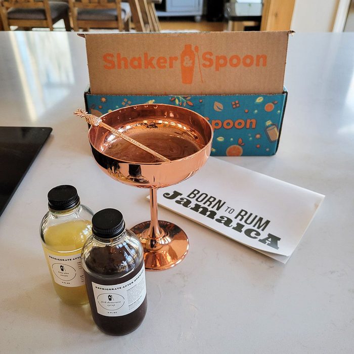Copper cocktail glass sits on a table, surrounded by two small bottles and a 