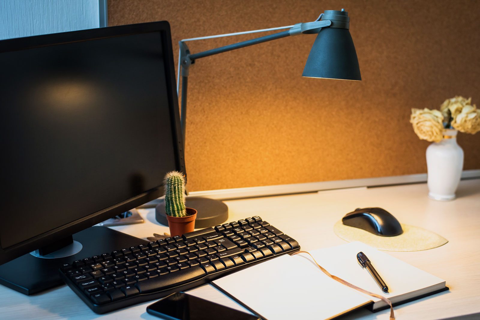 Desktop workspace in evening lighting with a lamp on near computer that has been shut down for the night