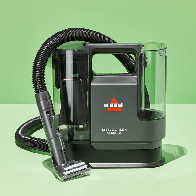A portable vacuum cleaner sits on a green surface with a visible hose, labeled 