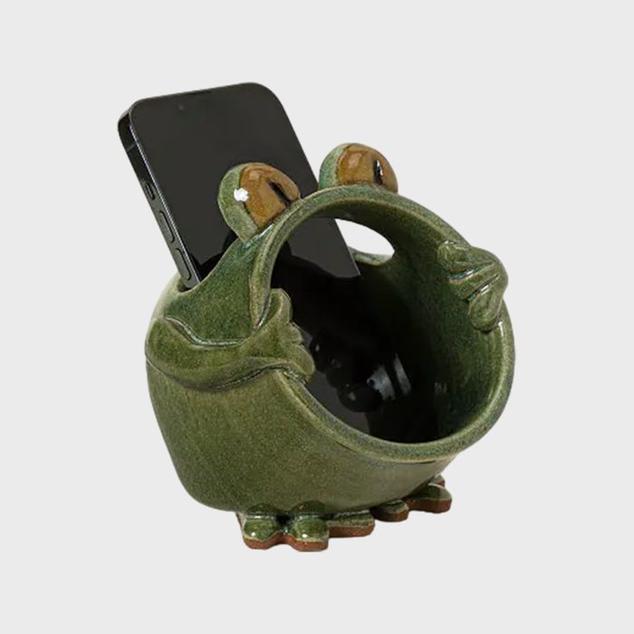 Ceramic frog holds smartphone, forming a whimsical phone stand. The frog appears playful with its open mouth and bulging eyes in a light background.