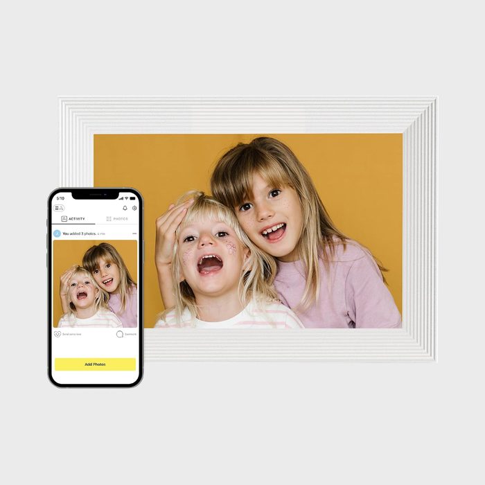 Two smiling children pose happily against a yellow background, with a smartphone displaying the same photo in front of the framed image.