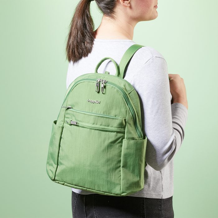 A green backpack hangs on a person's shoulder, standing sideways against a pale green background.