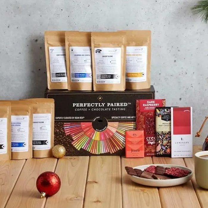 Coffee bags and chocolate bars are displayed together on a wooden table with holiday decorations, suggesting a coffee and chocolate tasting set.