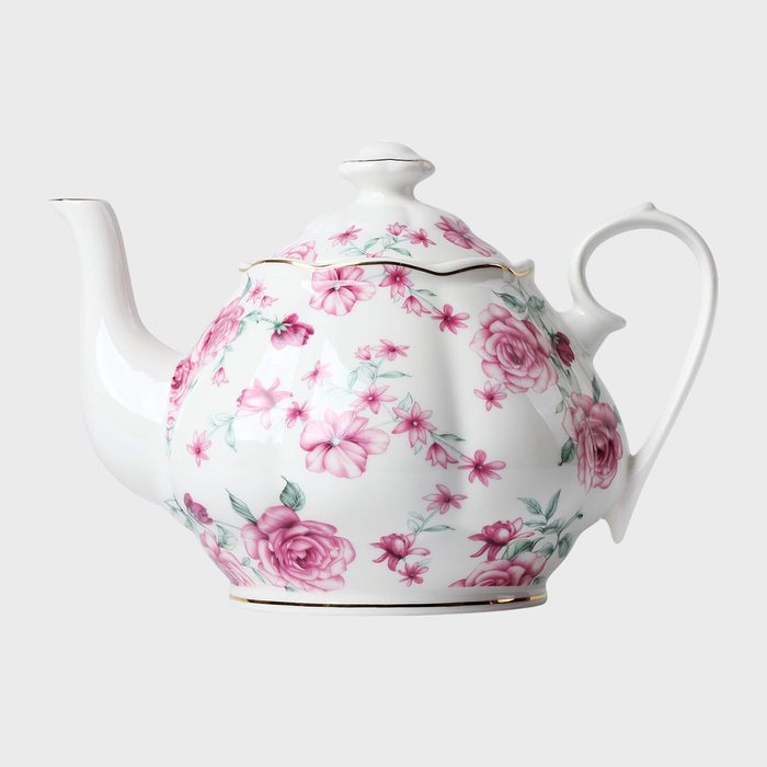 White porcelain teapot displaying pink floral patterns, resting in a plain, neutral background.