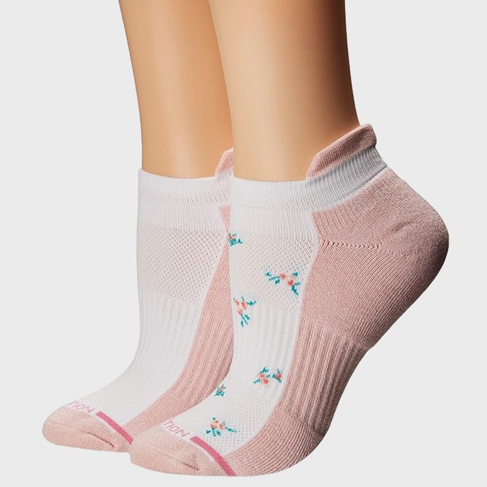Ankles wearing pink and white socks, featuring floral patterns, standing on a neutral background.
