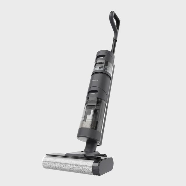Vacuum cleaner standing upright, handle angled backward, on a plain, light gray background.