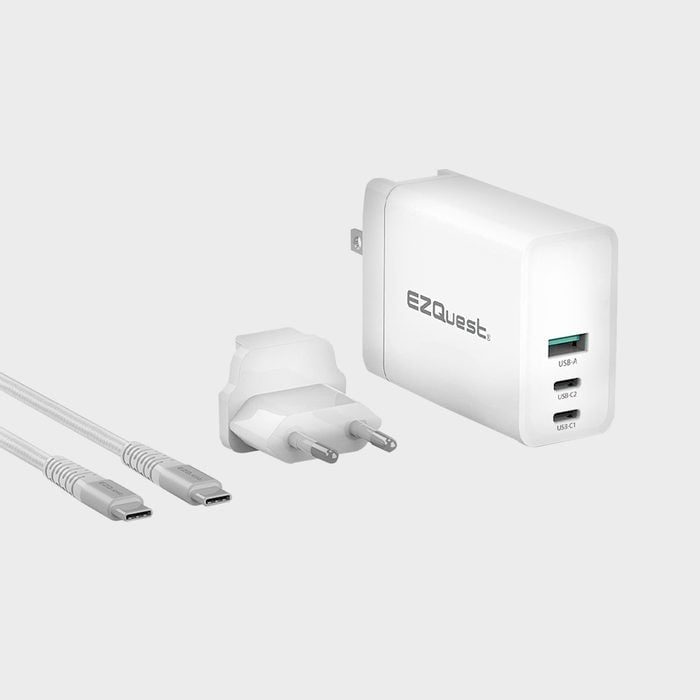 White charger with multiple ports, including USB-A and USB-C, resting near a plug adapter and two USB-C cables, set against a gray background.