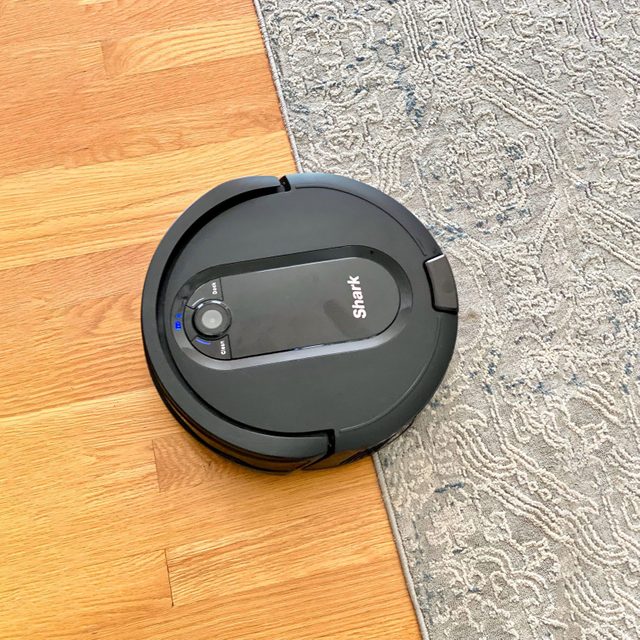 Robotic vacuum cleaner sweeps hardwood floor near patterned rug, displaying 