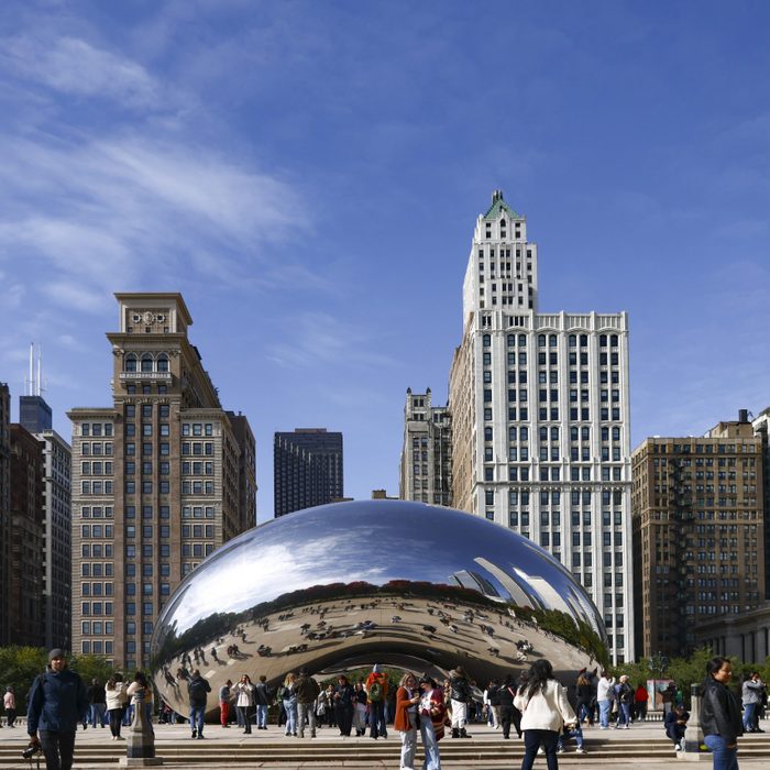 The sculpture reflects people and skyscrapers, surrounded by a city plaza with a clear blue sky.