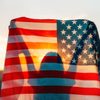 A person holds an American flag aloft against a sunset backdrop, creating a silhouette effect through the fabric.