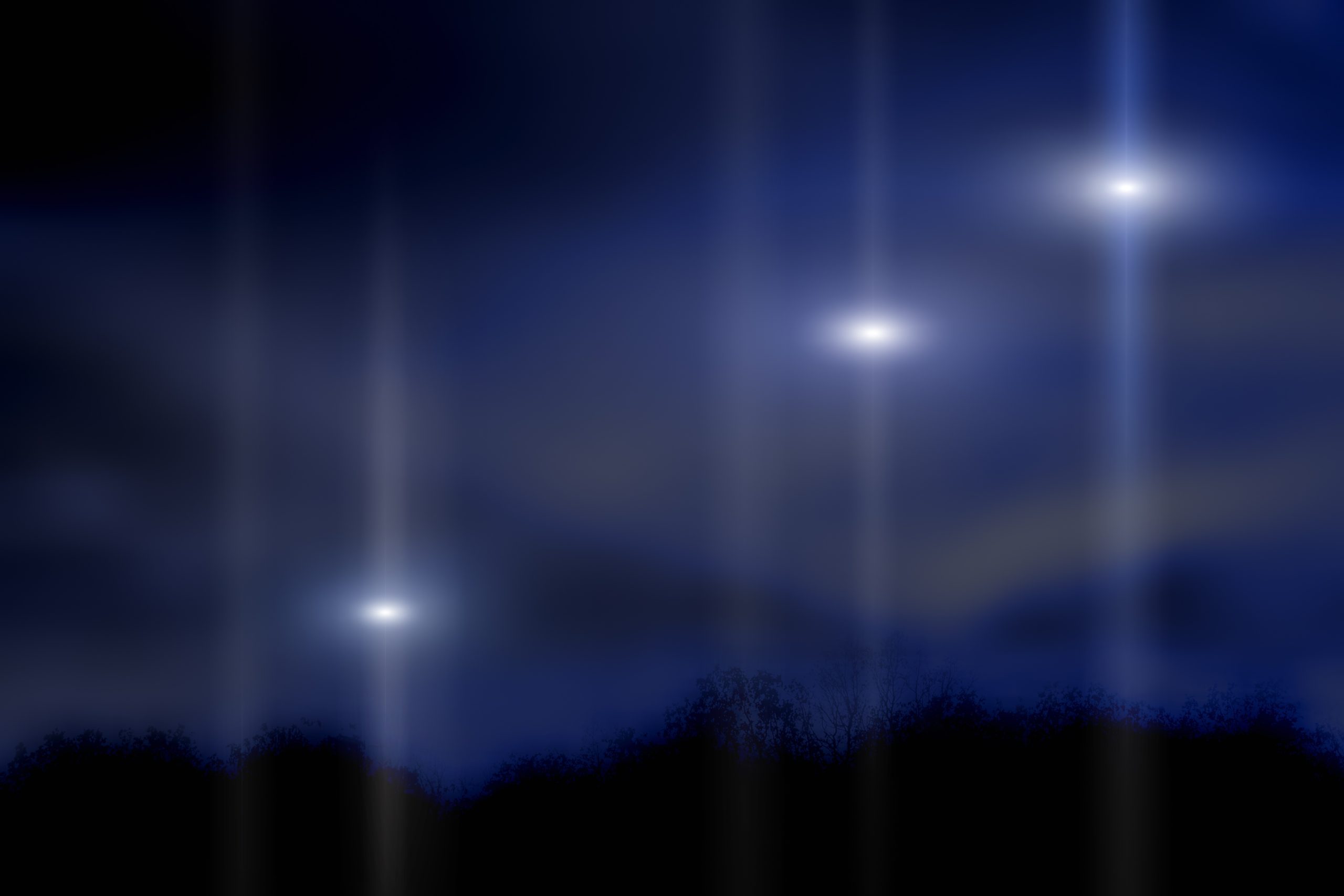 Three bright lights shine in the night sky above dark silhouetted trees, creating beams against a deep blue background.