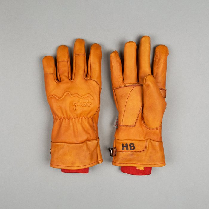 Two brown leather gloves rest side by side on a gray surface, featuring embroidered 