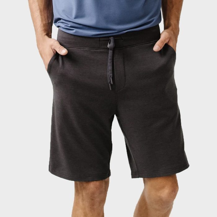 Person wearing dark shorts, hands in pockets, standing against a plain light background.