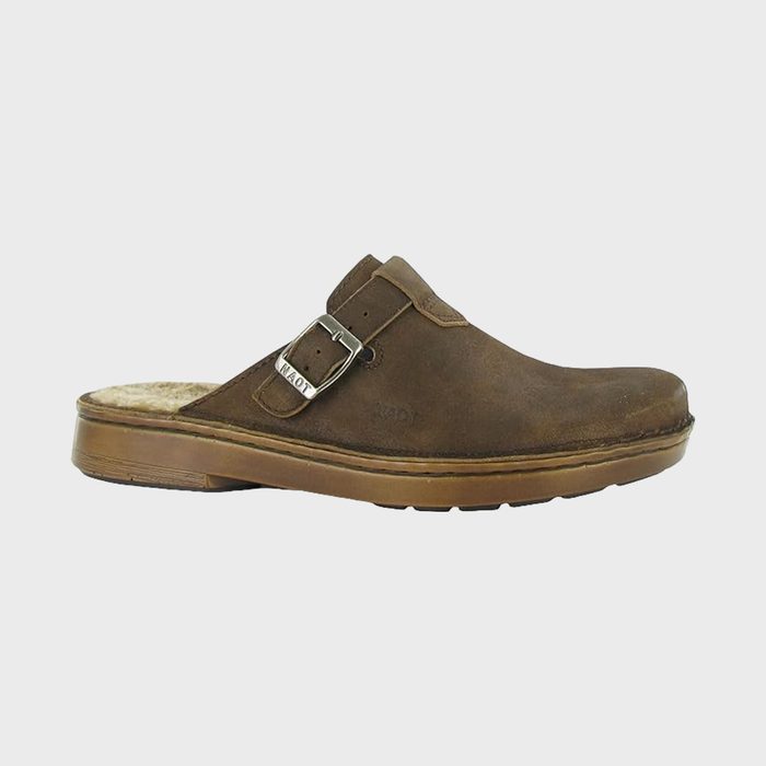 Brown leather clog shoe with adjustable buckle sits against a plain white background. The shoe features a thick sole and plush interior lining.