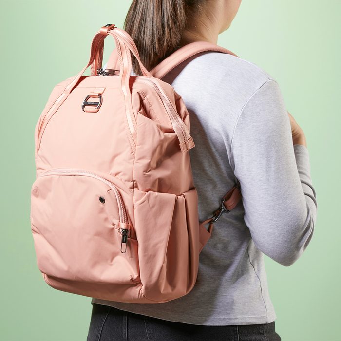 Pink backpack carried by person wearing a gray shirt, against a light green background.