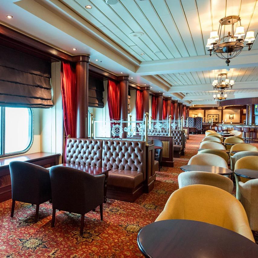Plush chairs and booths sit elegantly in a luxurious, warmly lit, vintage-style lounge with red curtains and patterned carpet.
