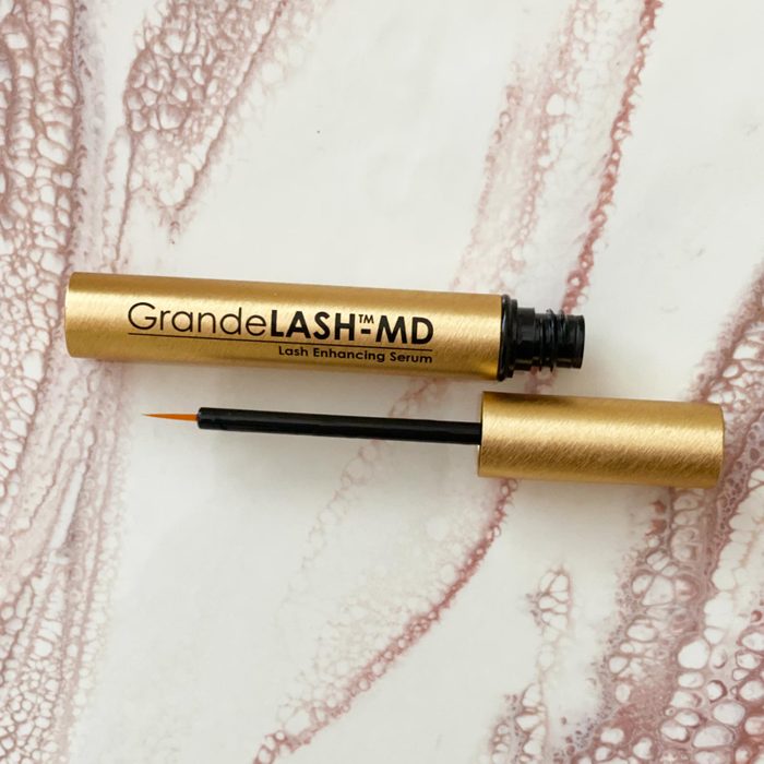 Tube lying open, showing a thin applicator brush; labeled 