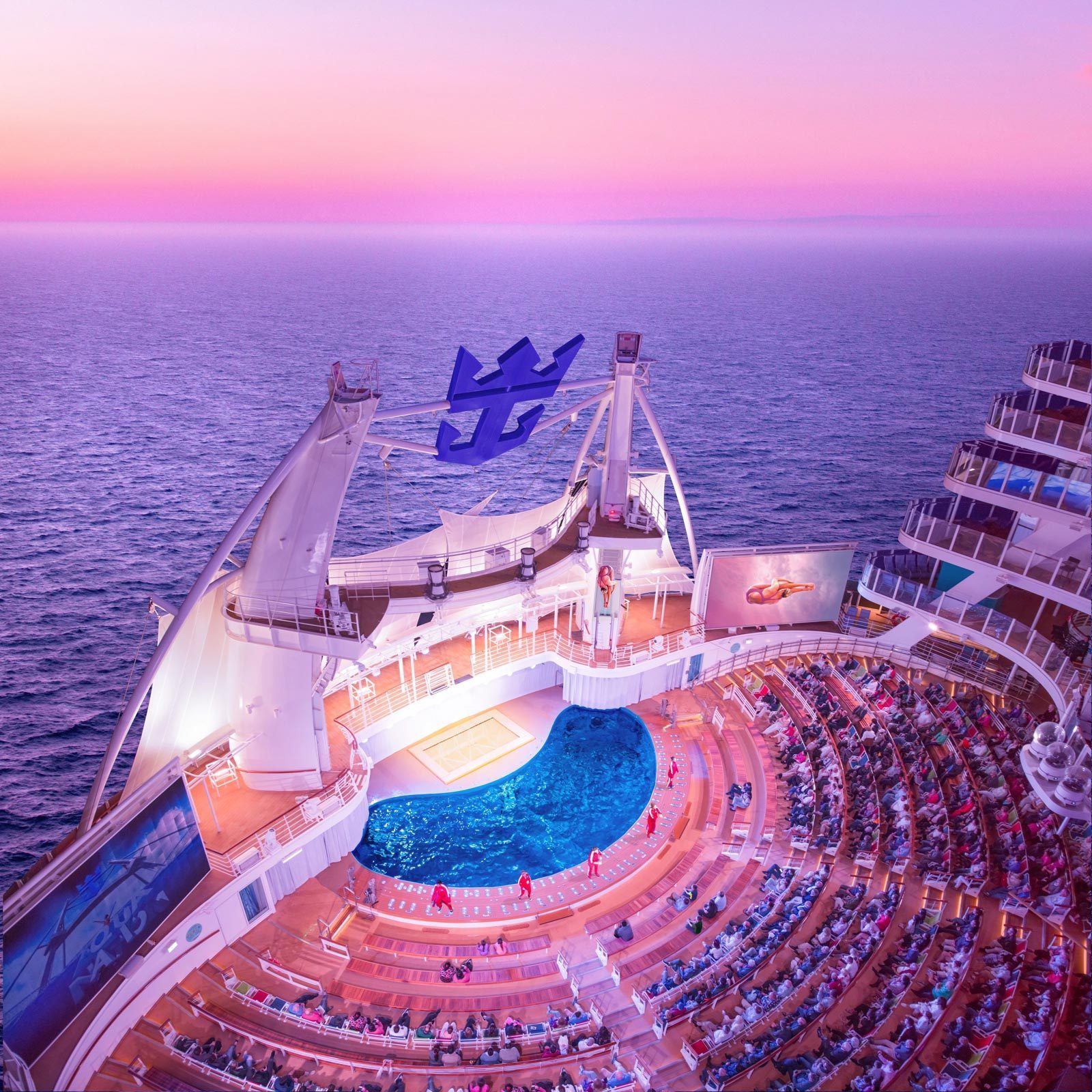 Amphitheater hosts a performance on a cruise ship, surrounded by the sea at sunset, with audience seated around a lit pool.