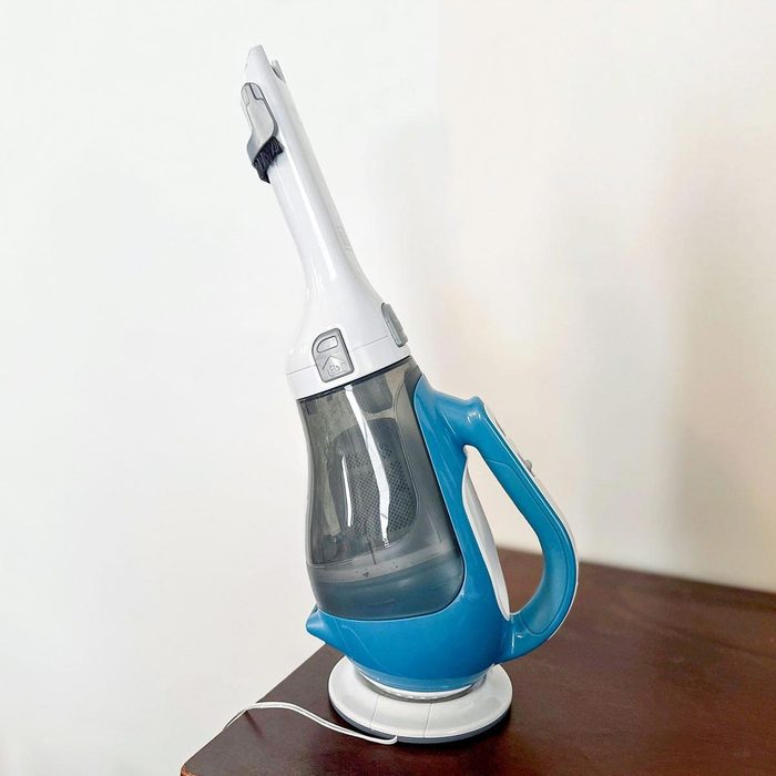 Cordless vacuum stands upright on a wooden surface, with blue and white accents in a minimalistic indoor setting.