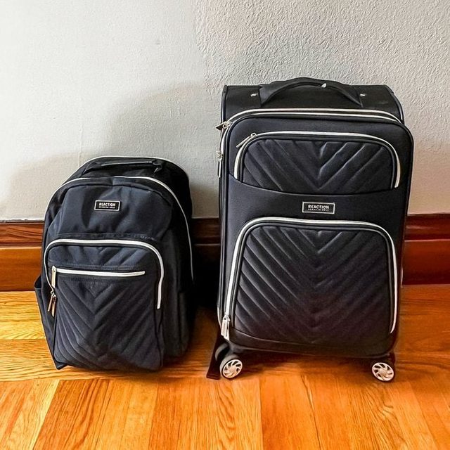 Backpack and rolling suitcase standing together on wooden floor, against a light-colored wall. Both are black with quilted patterns and silver zippers.