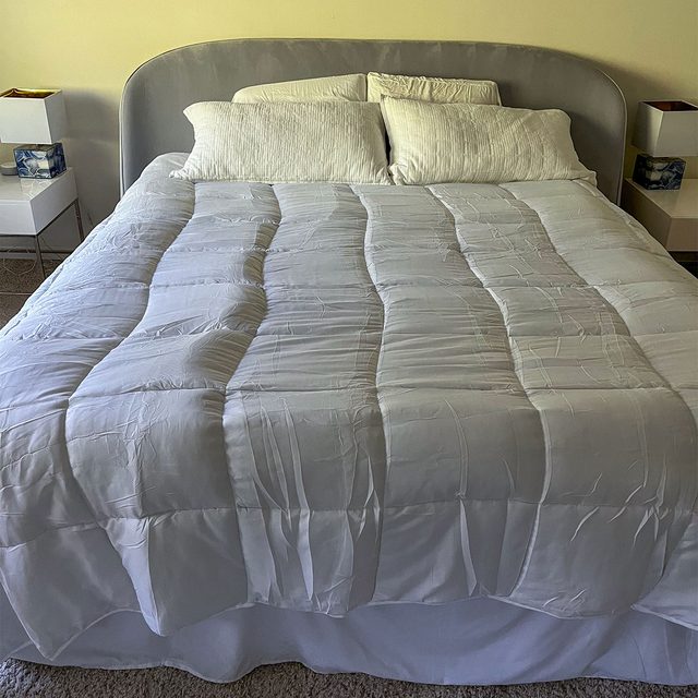 A neatly made bed with white pillows and comforter, flanked by modern white nightstands in a softly lit bedroom.