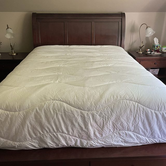 A neatly made bed with a white comforter sits between two nightstands with lamps in a cozy bedroom setting.