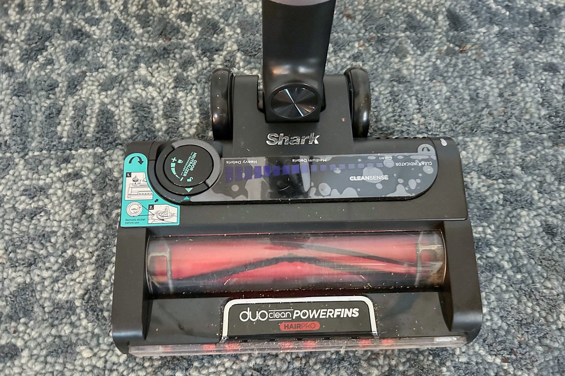 Vacuum cleaner head on carpet features rotating brush inside clear casing, with "Shark," "duo clean POWERFINS," and "CLEANSENSE" visible on the surface.