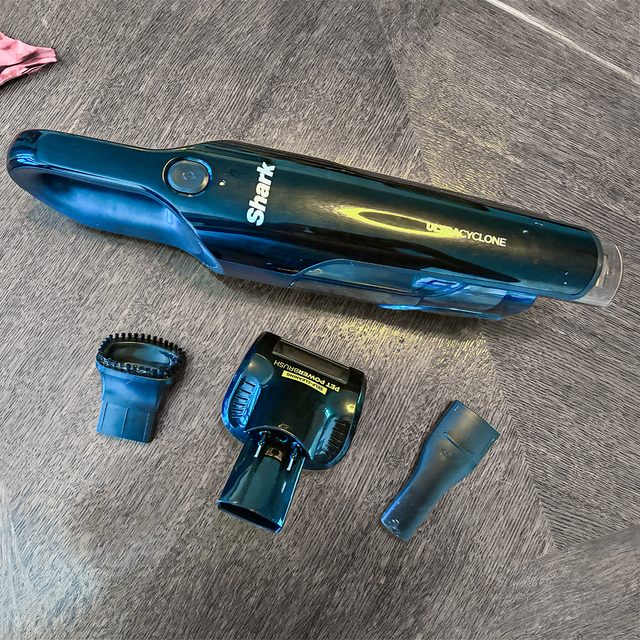 Handheld vacuum and attachments laying on a wooden floor, with 