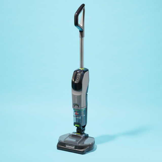 A vacuum cleaner stands upright on a light blue background, displaying the brand name 