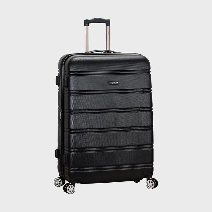 Black suitcase stands upright, featuring a retractable handle and four wheels. 