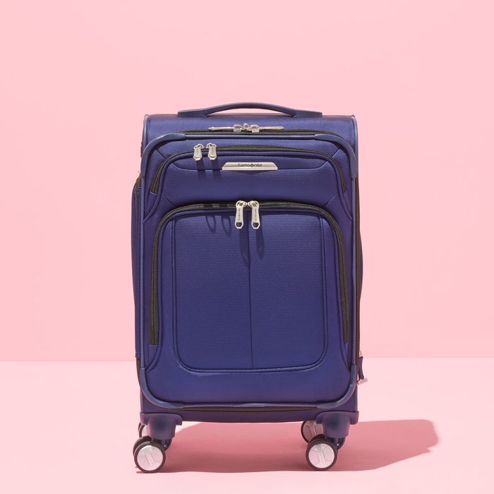 Blue suitcase stands upright on four wheels against a pink background.
