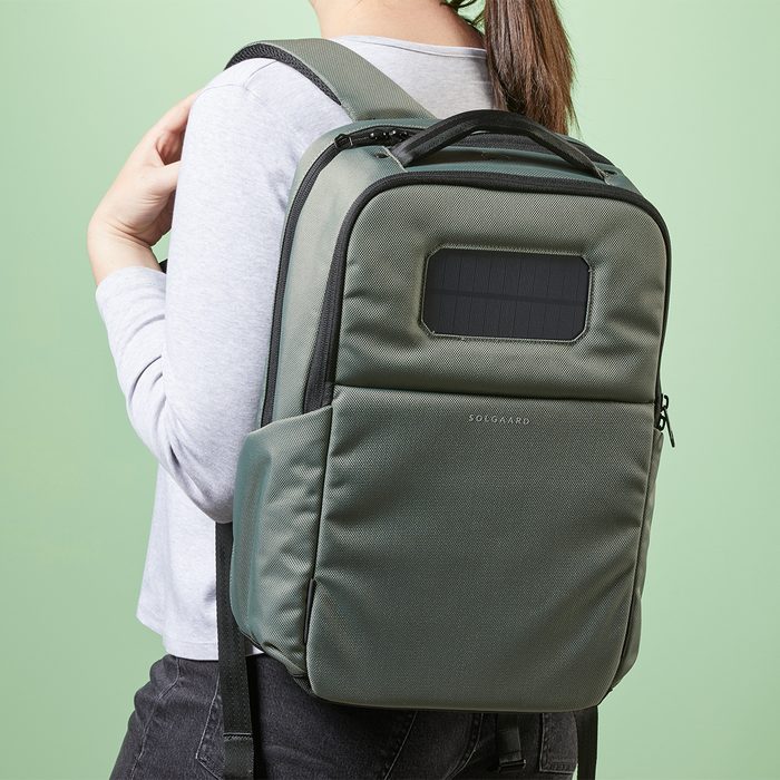 A green backpack with a solar panel is worn by a person in a gray shirt against a light green background.