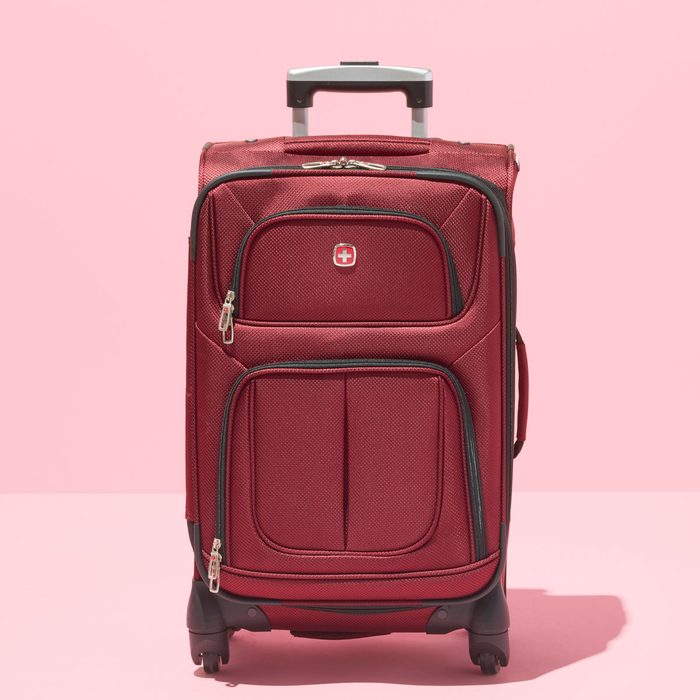 Red suitcase stands on pink background, displaying multiple zippered compartments and a telescopic handle.