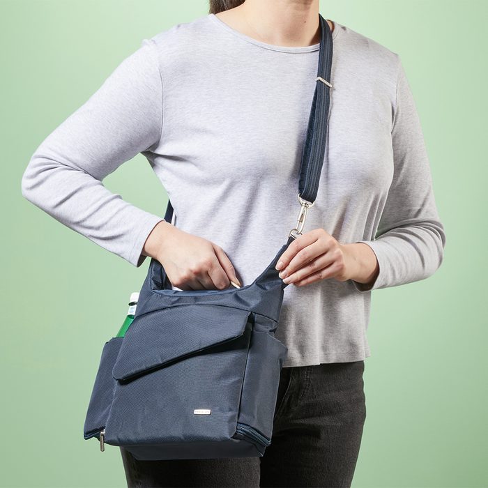 A navy bag is worn across the body, with a person placing a hand inside; light green background.