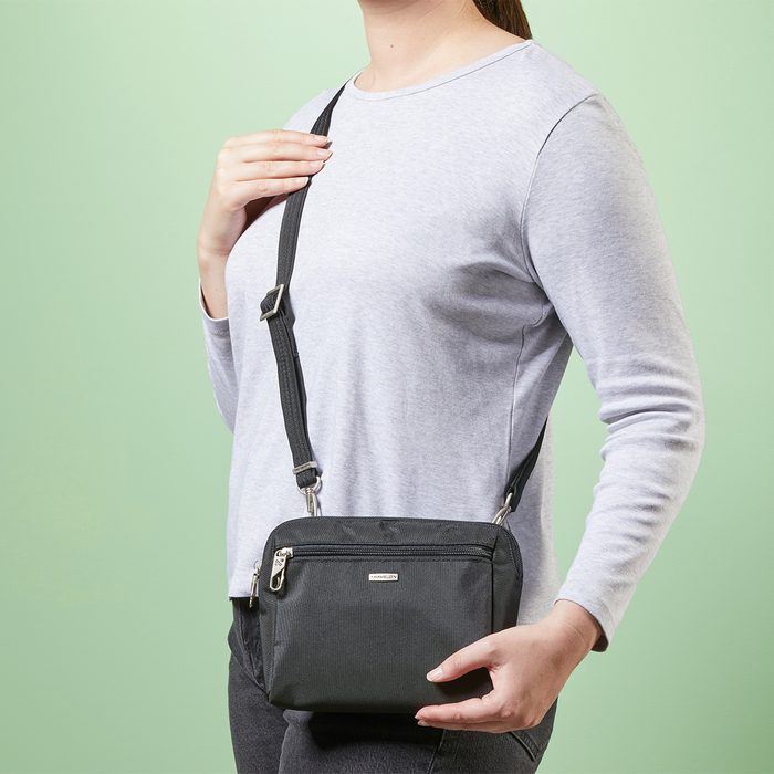 Person holds a small, black shoulder bag; wearing a light gray sweater against a light green background.